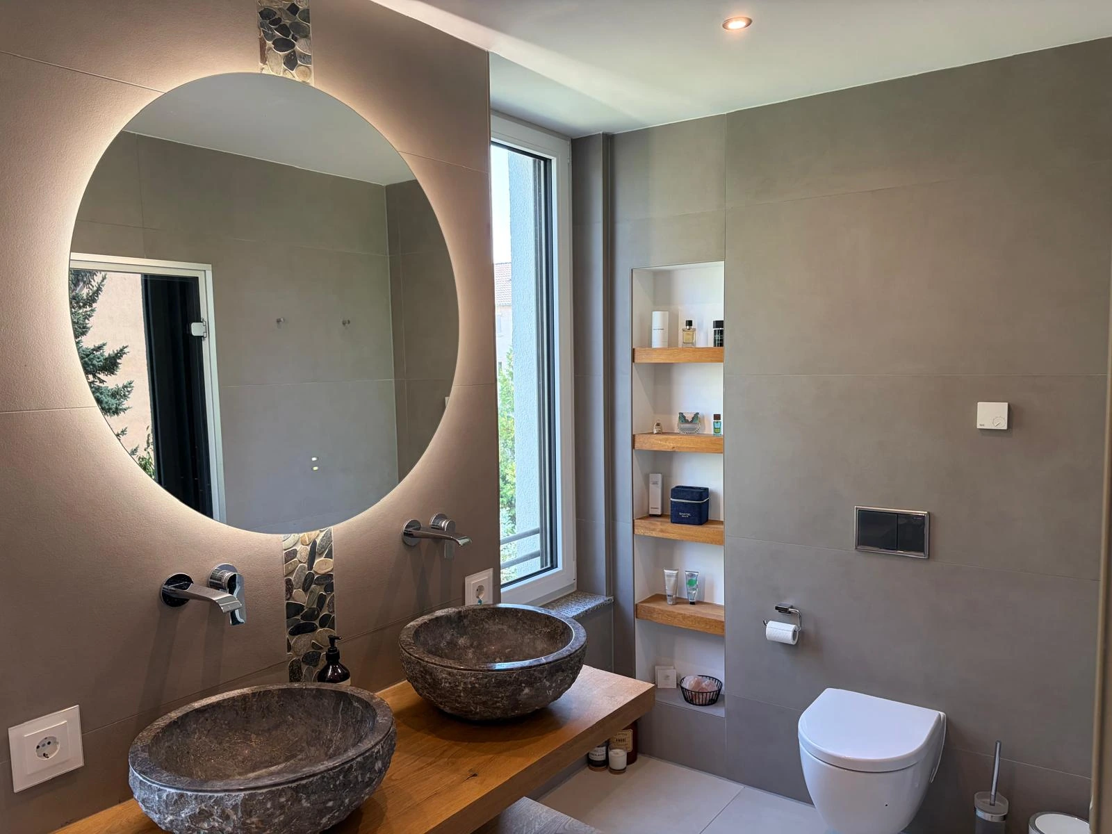 Badezimmer mit Doppelwaschbecken aus Stein, rundem Spiegel und WC